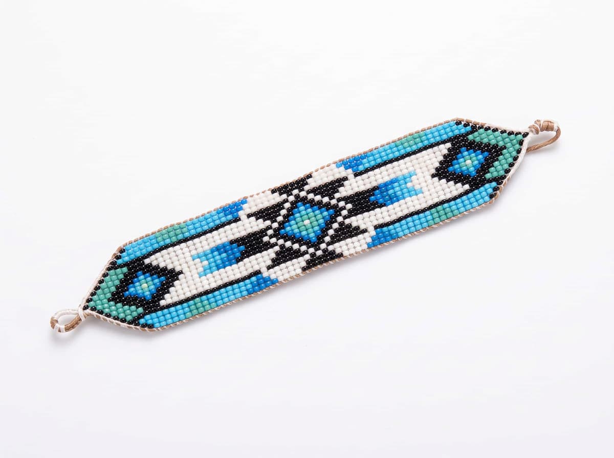 Closeup of a handmade wide blue and turquoise beaded cuff bracelet with ethnic geometric patterns on a natural linen cloth with dried eucalyptus