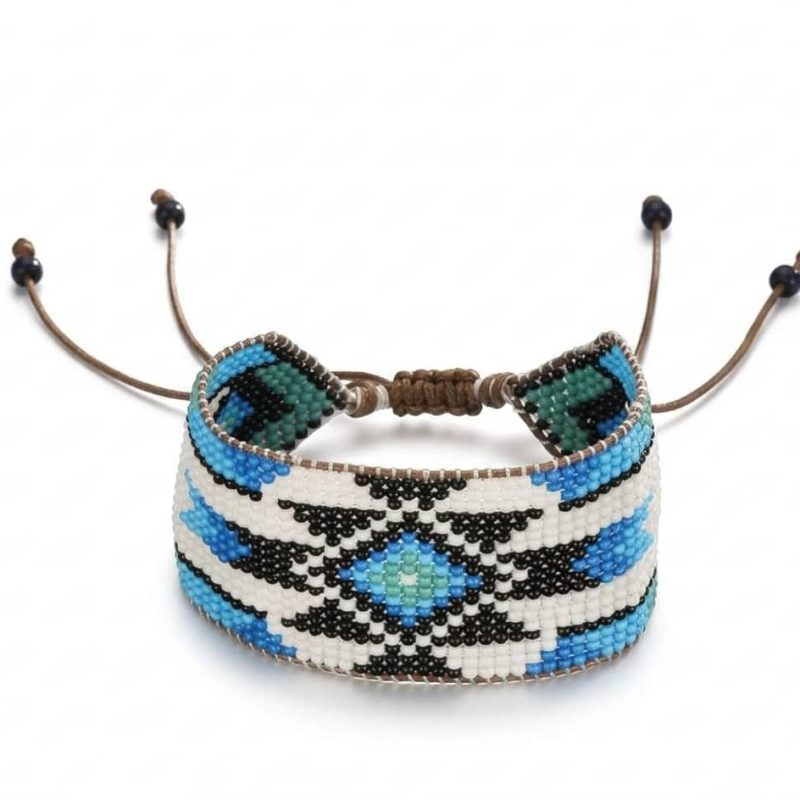 Closeup of a handmade wide blue and turquoise beaded cuff bracelet with ethnic geometric patterns on a natural linen cloth with dried eucalyptus.