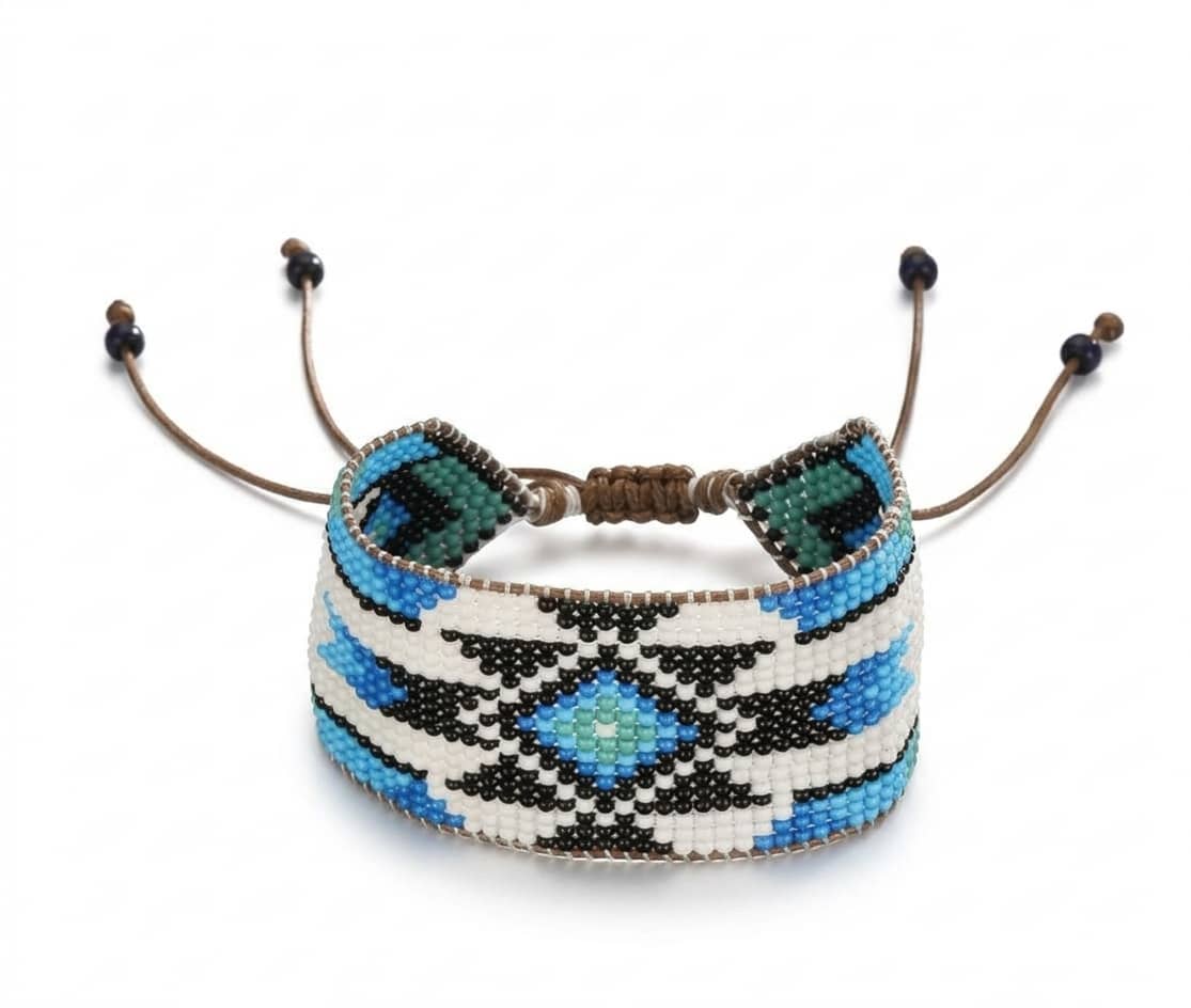 Closeup of a handmade wide blue and turquoise beaded cuff bracelet with ethnic geometric patterns on a natural linen cloth with dried eucalyptus.