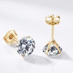 Pair of solid 14K gold stud earrings with 0.5 carat round brilliant moissanite stones (1.0 CTW) displayed in an emerald green velvet box beside a JEWELRY KOVAL card